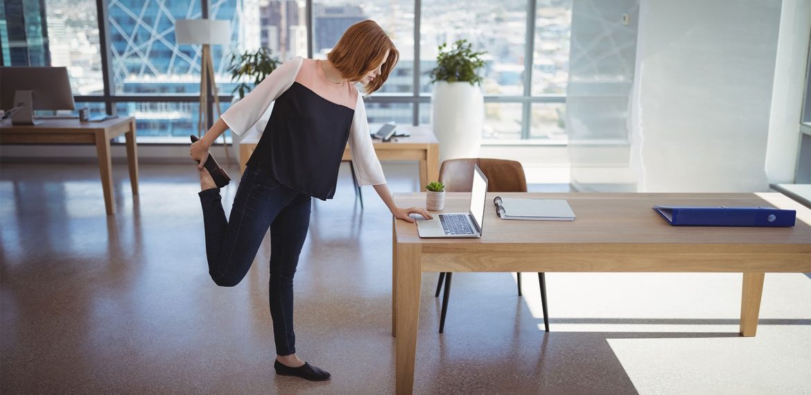 Mulher alonga a perna enquanto trabalha dentro do escritório